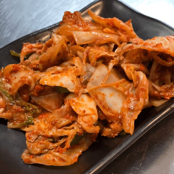A close-up of a black rectangular plate filled with spicy, red kimchi.