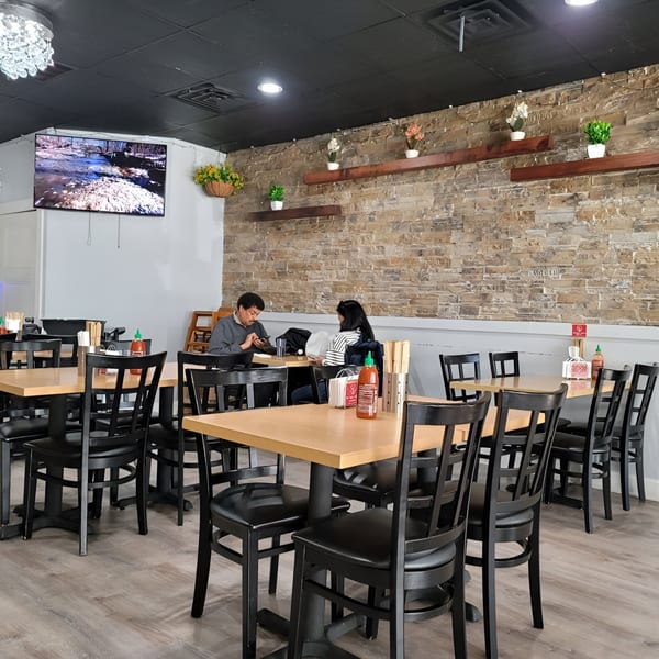 Interior of Momoyama Ramen & Hawaiian BBQ with customers dining at light wood tables and black chairs.