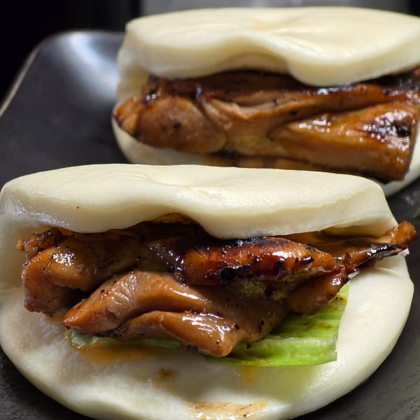 Two Momoyama Ramen & Hawaiian BBQ chicken bao buns with lettuce on a dark plate.