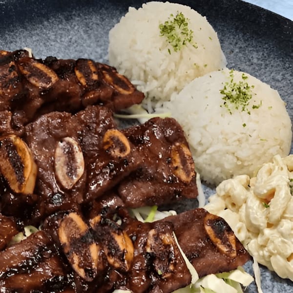 Momoyama Ramen & Hawaiian BBQ's Kalbi ribs, two scoops of rice, and macaroni salad on a dark plate.