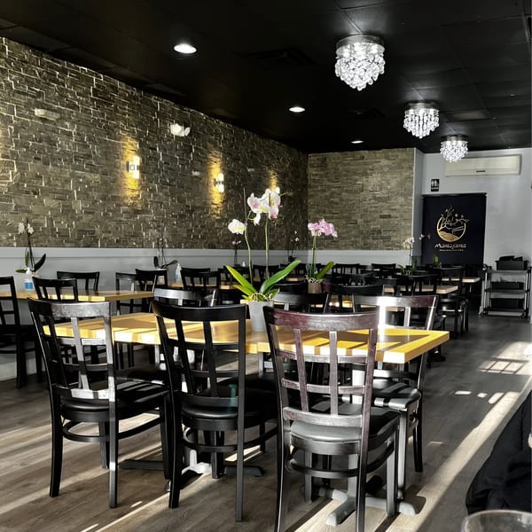 Interior of Momoyama Ramen & Hawaiian BBQ with empty tables, black chairs, stone wall, and orchid centerpieces.