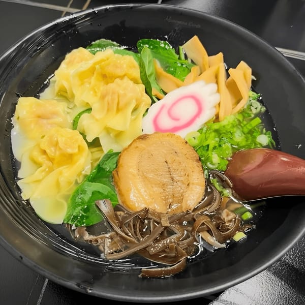 Close-up of a Momoyama Ramen bowl with wontons, pork, fish cake, bamboo, and green onions.
